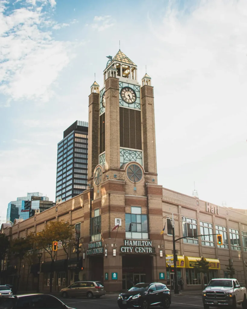A prominent clock tower at Hamilton, Ontario City Centre with a brick facade, surrounded by modern skyscrapers and busy streets with cars.