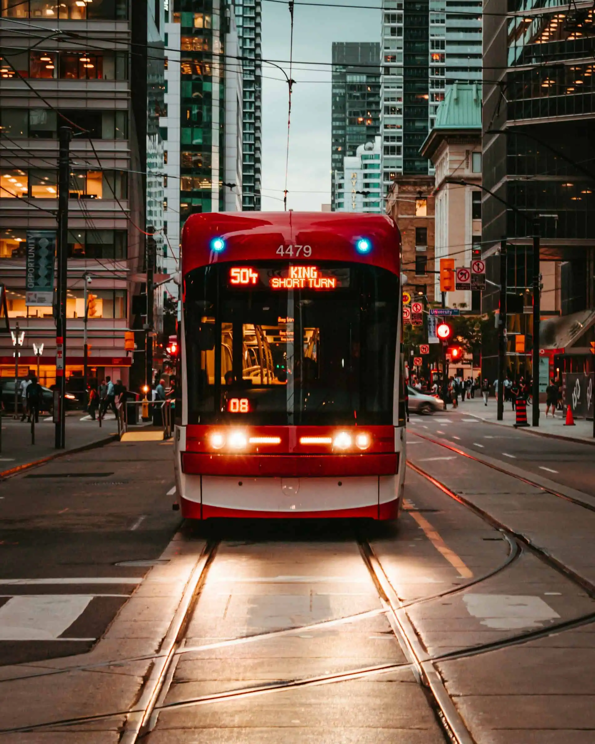 A red Toronto streetcar on the 504 King route traveling through a bustling downtown area with modern skyscrapers and illuminated streets at night.